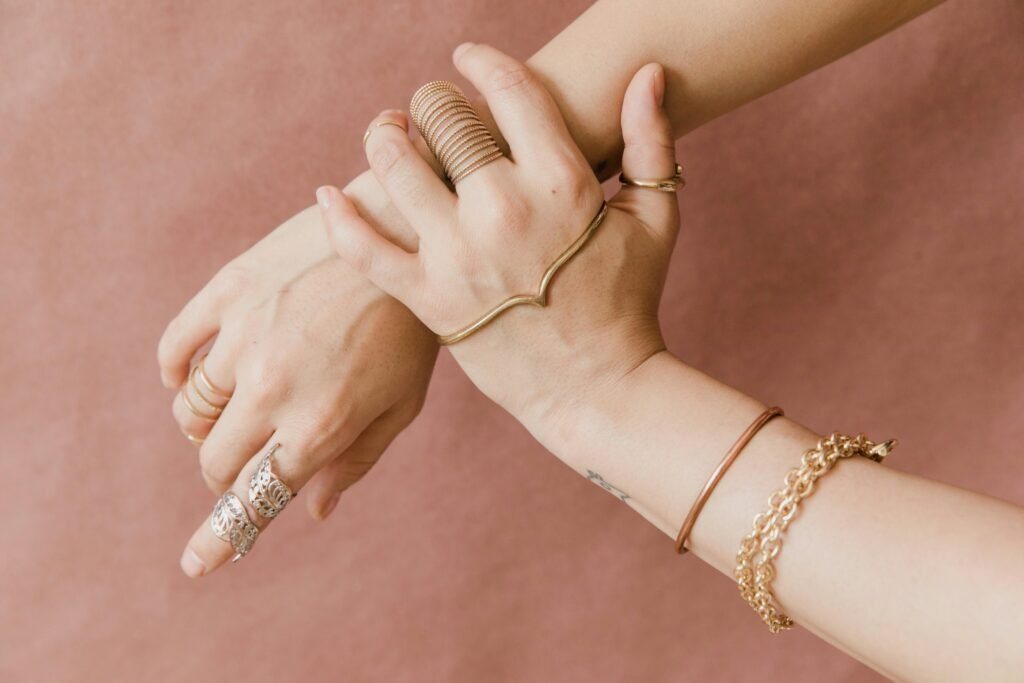 Elegant hands adorned with gold jewelry against a soft pink background, showcasing style and grace.